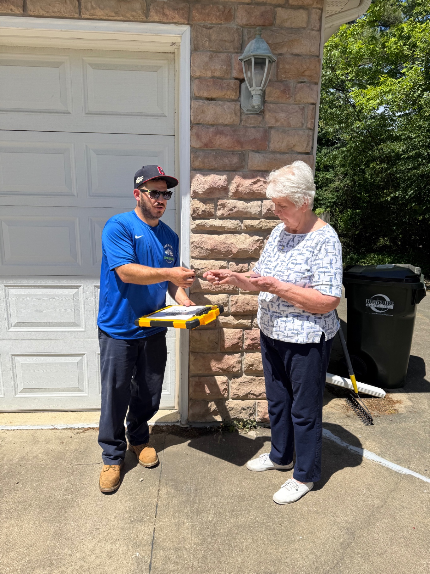 The Best Junk Removal LLC owner Andy handing a paid receipt to a senior homeowner after an upfront-priced driveway and garage cleanout in Greater Cleveland, Ohio — locally owned, trusted, no hidden fees