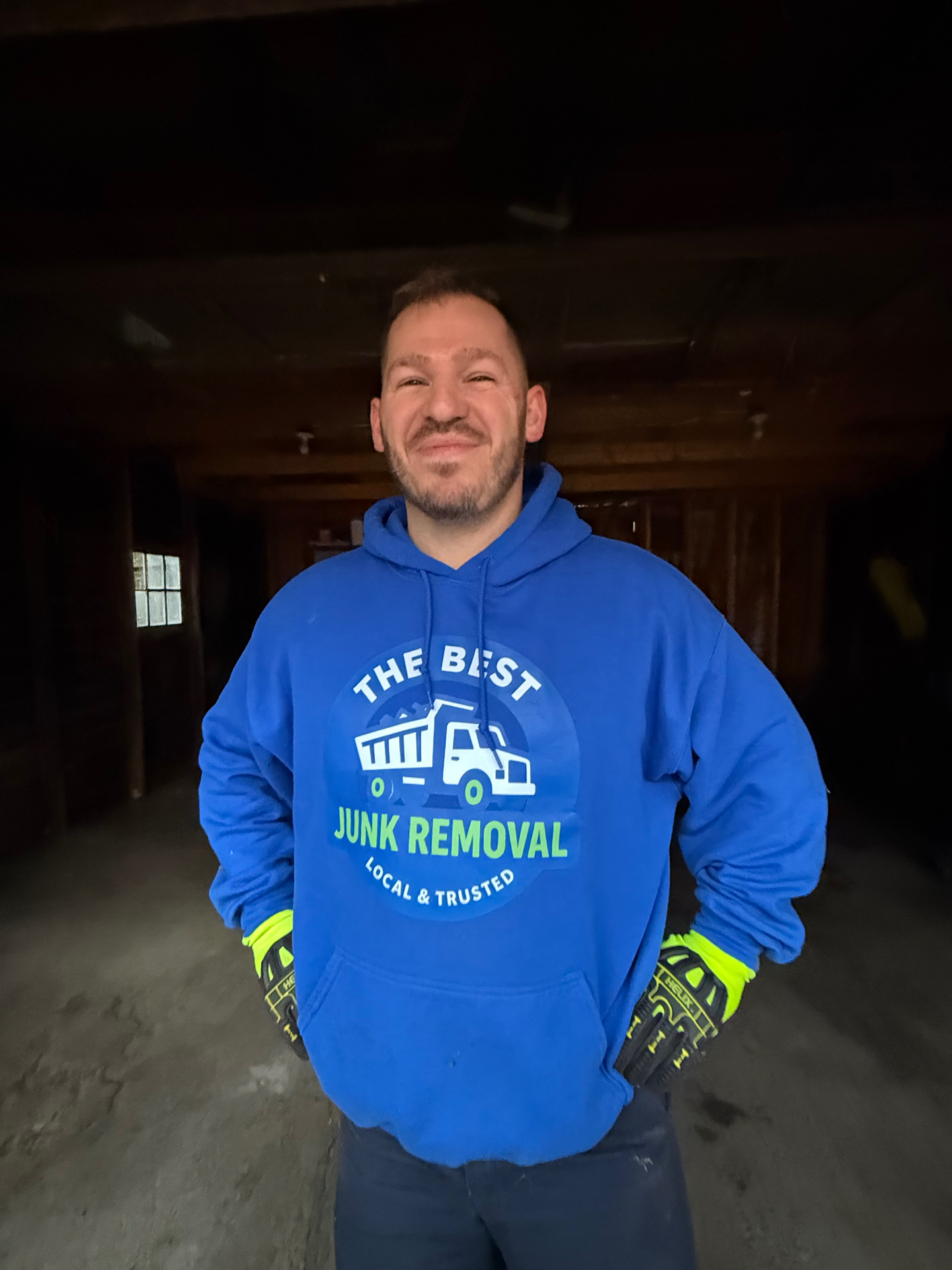 Andy, owner of The Best Junk Removal, wearing a branded blue TheBestJunk hoodie and work gloves inside a Cleveland basement cleanout